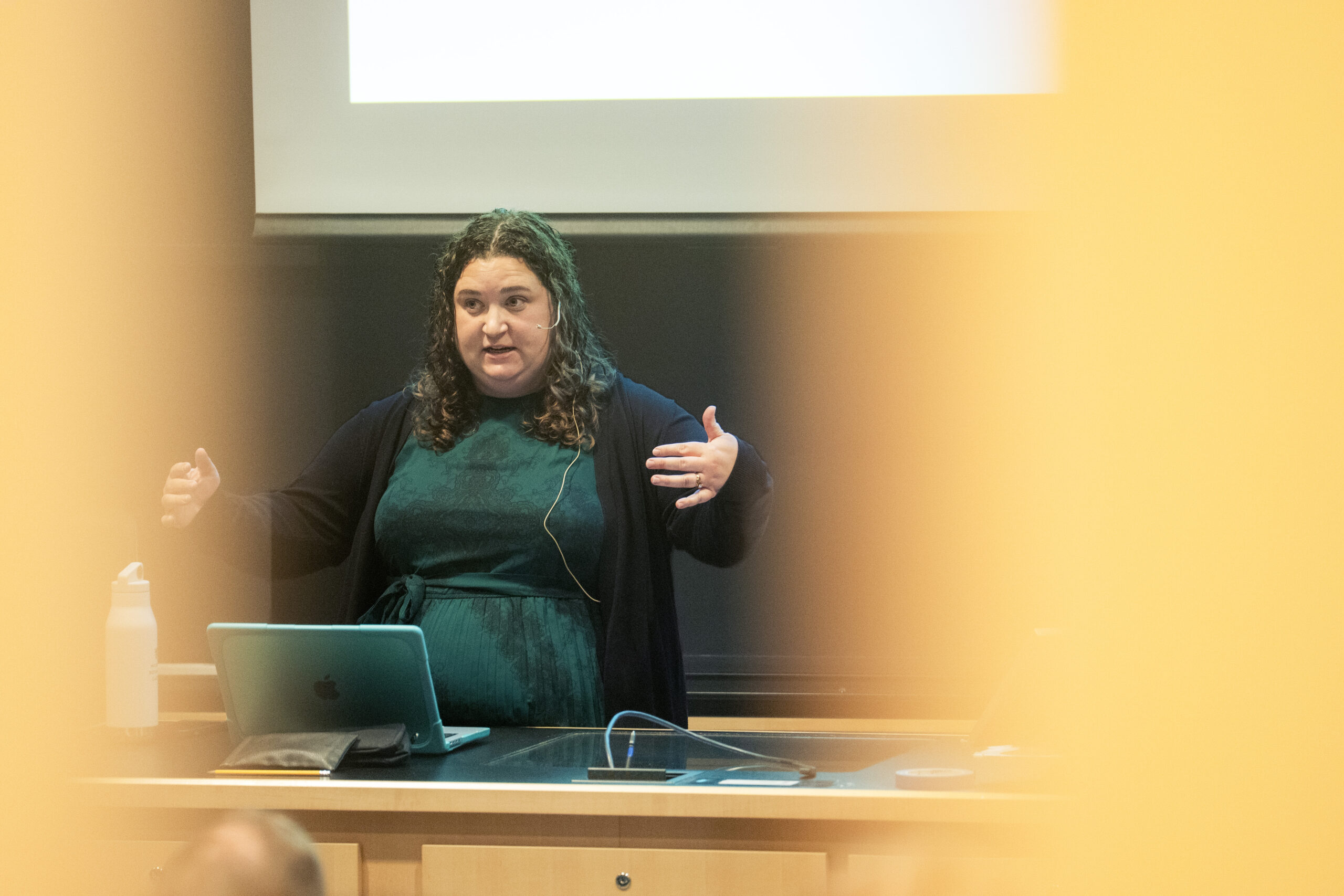 A woman stands before a whiteboard giving a lecture